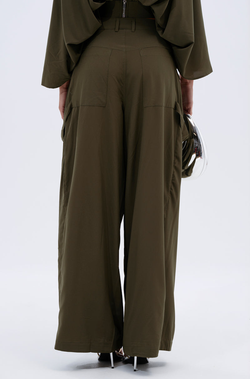 Someone stands with their back to the camera, holding a helmet and wearing the TALK ABOUT ME TROUSER—loose-fitting, high-rise olive green pants with wide legs and patch pockets for a utilitarian style. 5