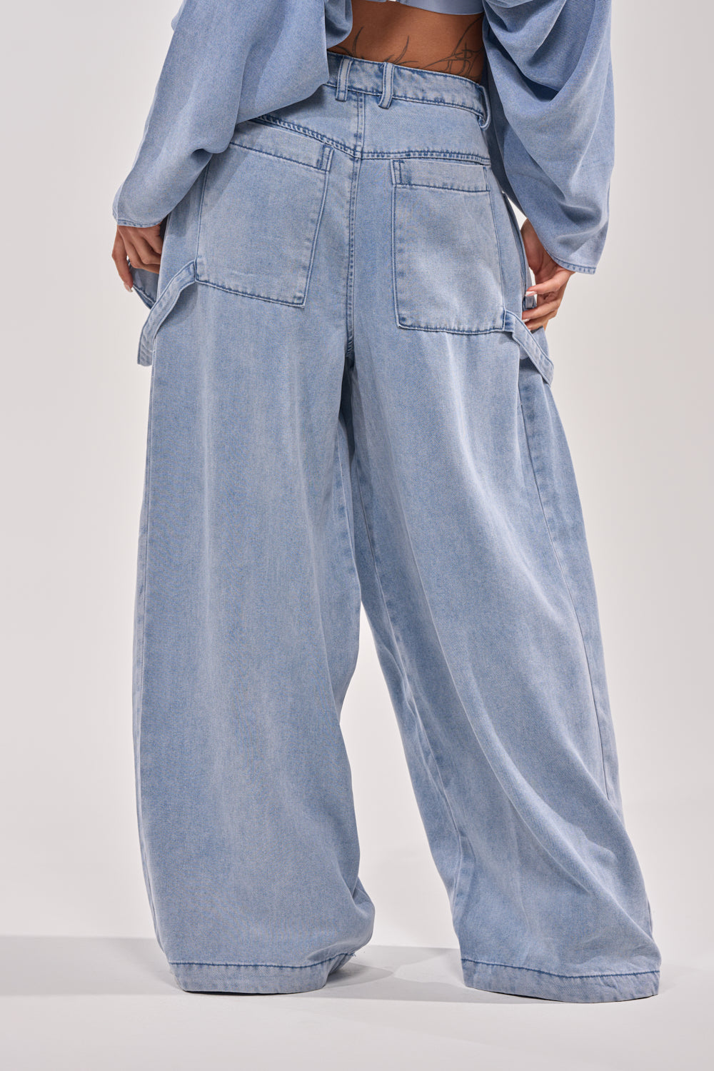 A person is shown from the back wearing DRIFTING AWAY CARGO DENIM pants and a matching top, featuring wide legs, large back pockets, and a relaxed streetwear-inspired fit. 4