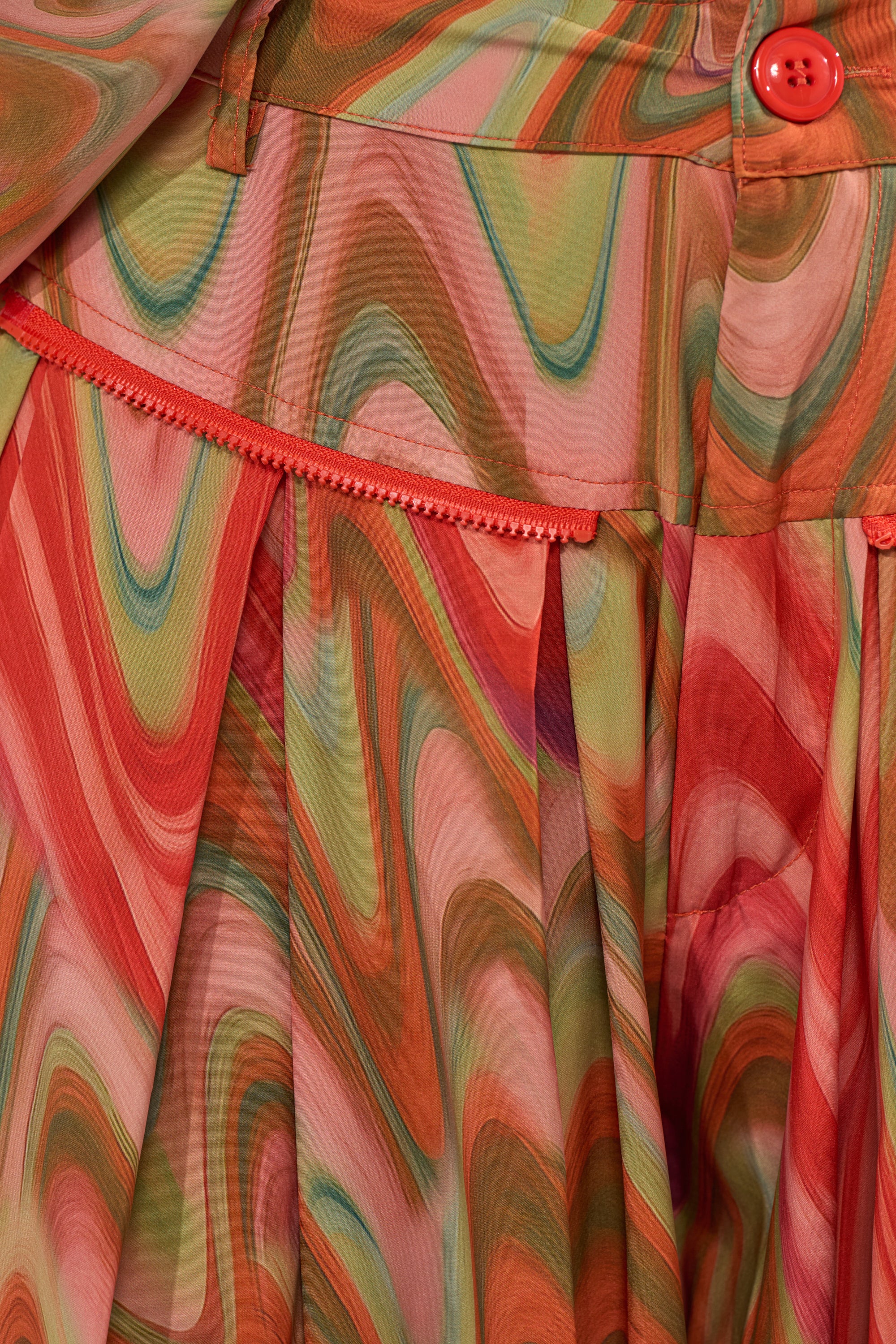 Close-up of the DRIFTING AWAY TROUSER’s vibrant swirl print in red, orange, green, and pink. Features a high waistband with pleats, red button, and decorative trim—ideal for standout street style. 9