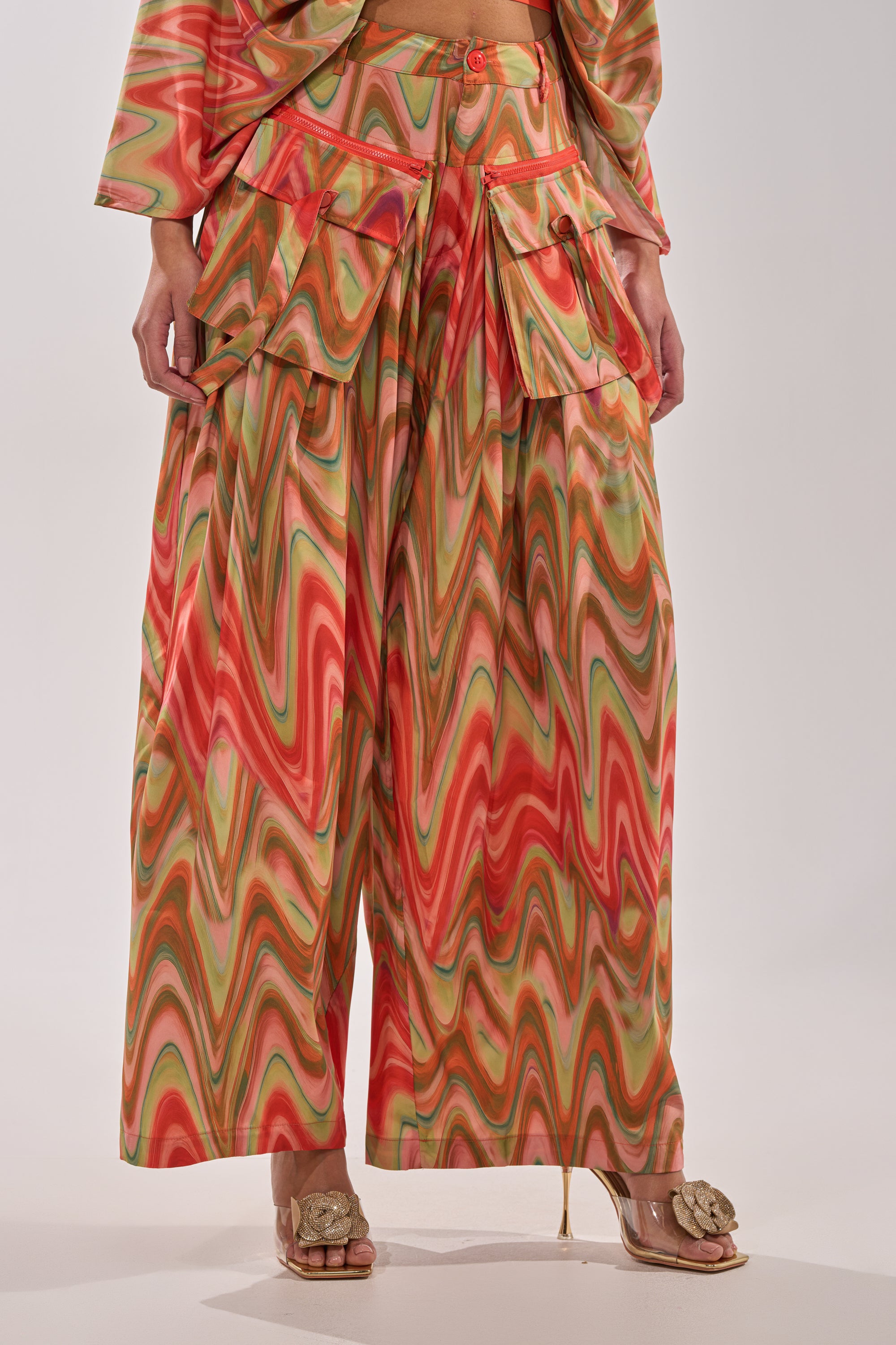 Wearing the DRIFTING AWAY TROUSER—high-waisted, wide-leg cargo pants with an abstract swirl print in red, green, and beige—styled with open-toe bow heels for a standout street style look. 2
