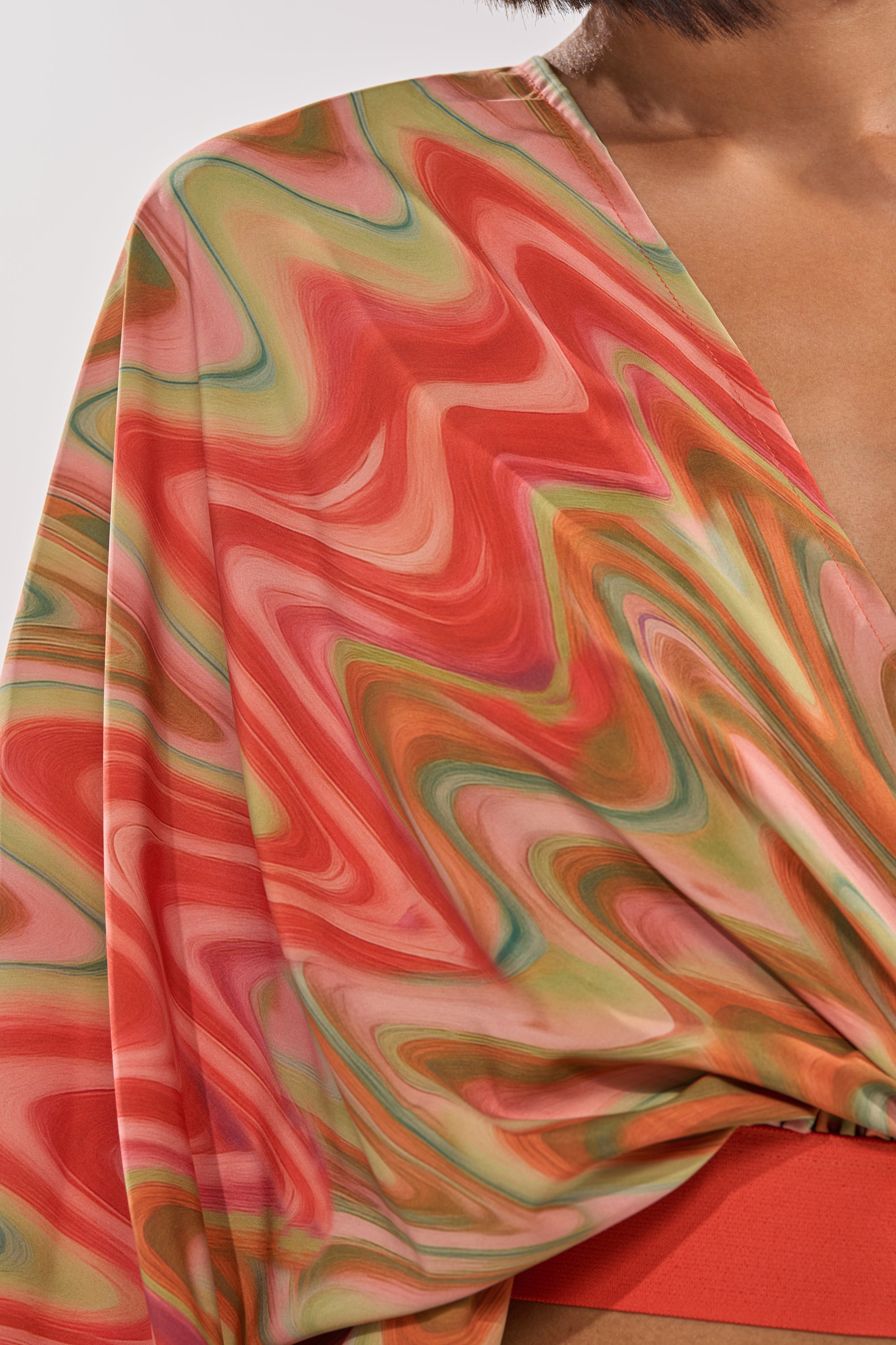 The DRIFTING AWAY BLOUSE is an abstract swirl wrap top in sunset hues, showcasing a colorful marble pattern, V-neckline, and draped fabric. 6