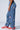 A person is sporting the COUNT IT UP! WIDE LEG JOGGERS in blue, adorned with colorful embroidered numbers ranging from 1 to 8 that are scattered randomly. These high-rise joggers feature a loose fit, an elastic waistband, and a wide-leg silhouette. They complete the look with red sneakers.