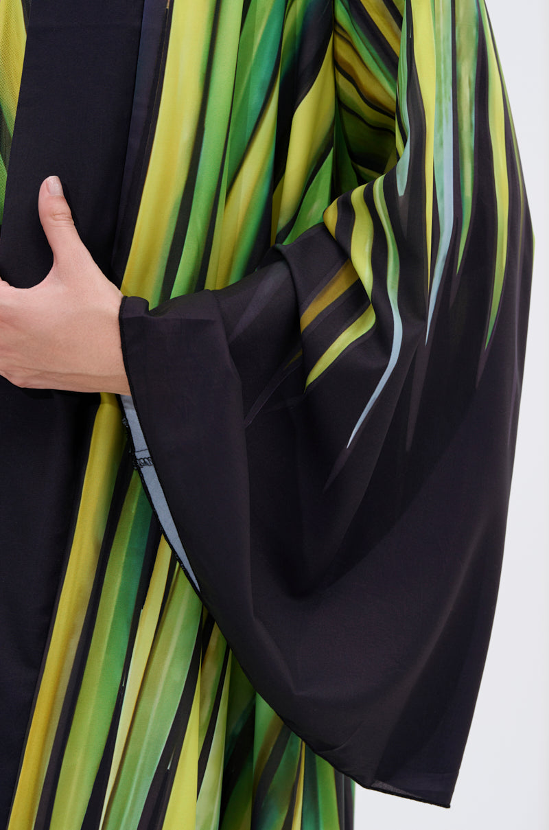 A close-up shows someone wearing the DEEP IN THE WOODS DUSTER with black, yellow, and green stripes. The satin fabric has a subtle sheen as they gently hold it near the chest against a plain, light background.