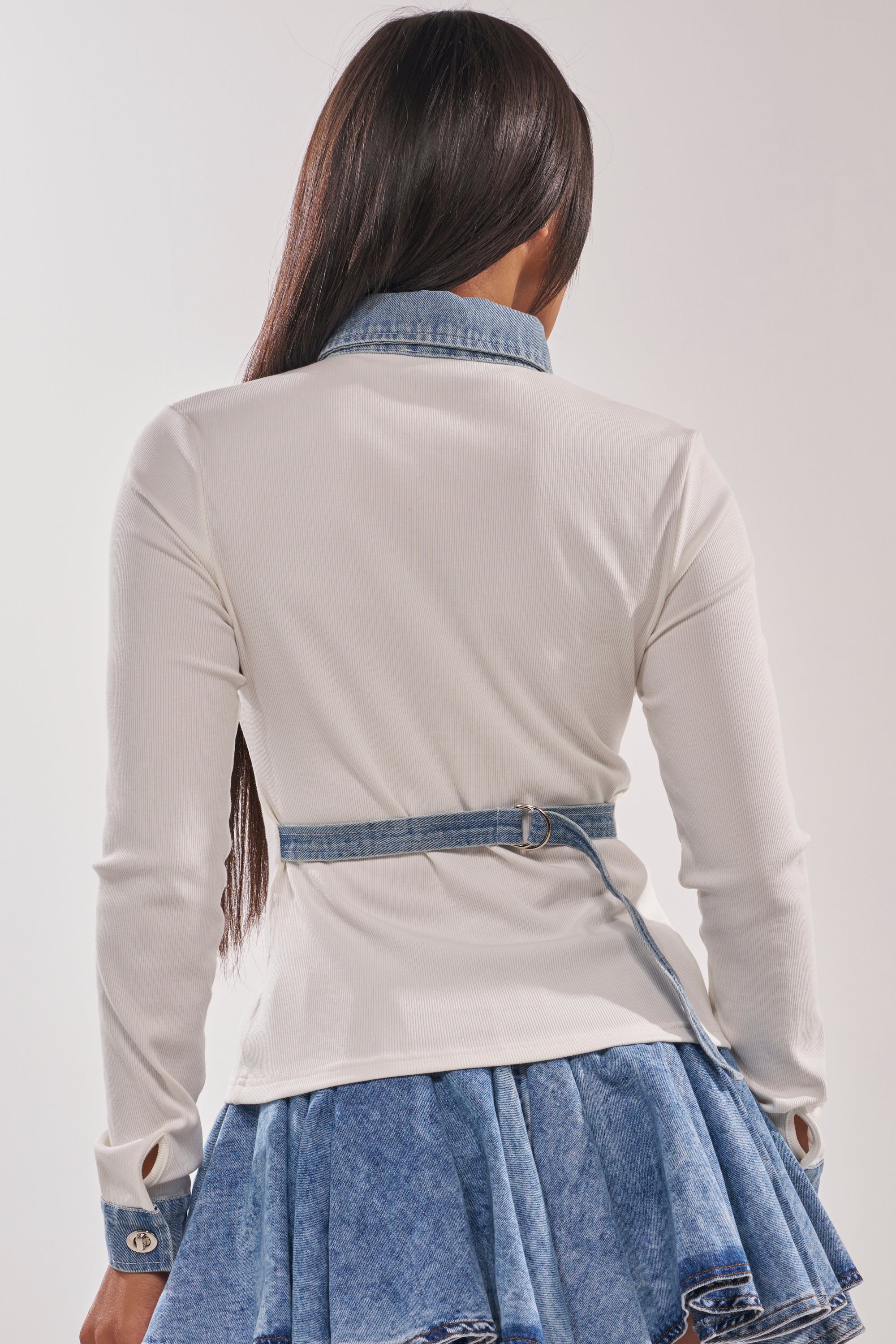 A woman with long dark hair is shown from the back, wearing the SHANNON KNIT BUTTON DOWN IN WHITE, styled with a blue denim pleated skirt. 6