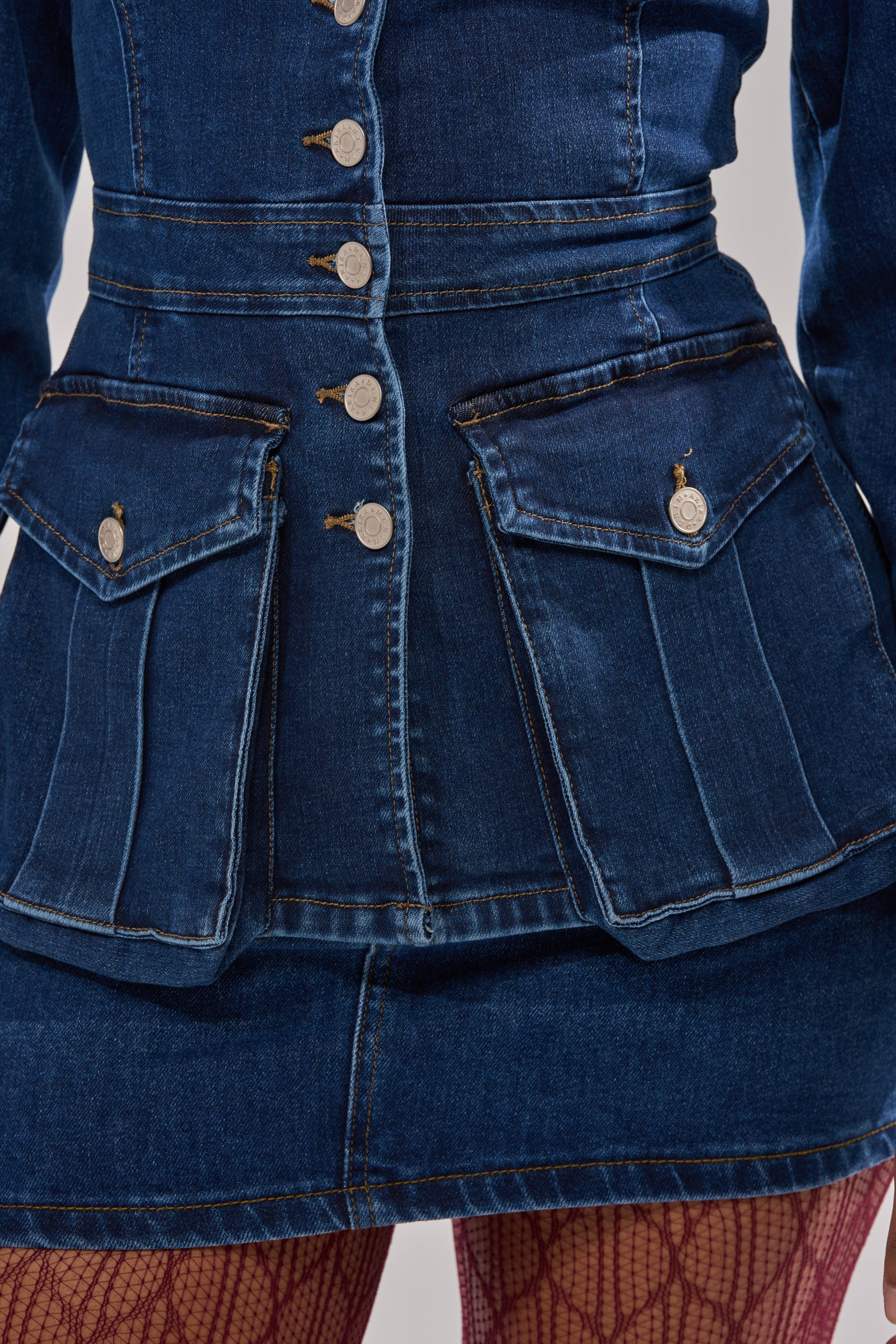 Close-up of a person wearing the CRAZY FOR YOU LONG SLEEVE DENIM BUTTON DOWN with large front pockets and silver buttons, styled with a matching denim skirt and red fishnet tights.