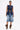 A woman faces forward in the UMI STRETCH DENIM TOP with high-shine gold hardware, paired with knee-length wide denim shorts, leopard print slouch boots, and sunglasses. Hair pulled back and a neutral expression complete her utility-chic look.