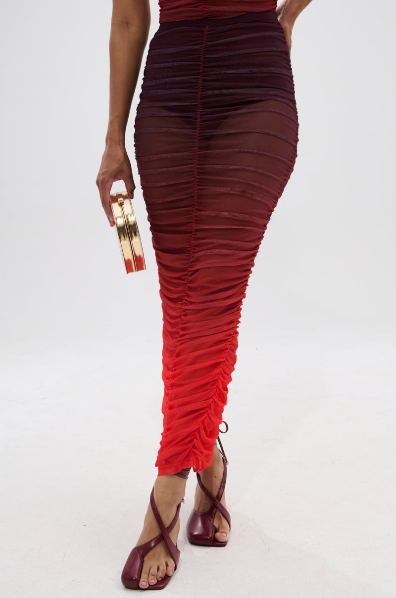 Wearing the OH FIRE OMBRE MAXI SKIRT with ruched detailing, purple strappy heels, and a small gold clutch, a person stands against a plain white background.