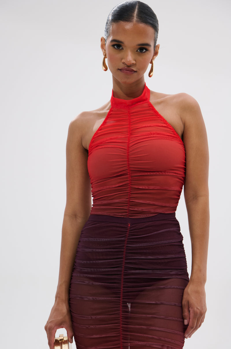 A woman stands against a plain light background wearing the OH FIRE OMBRE MESH BODYSUIT, accented with gold hoop earrings and a small purse for a bold, standout look.