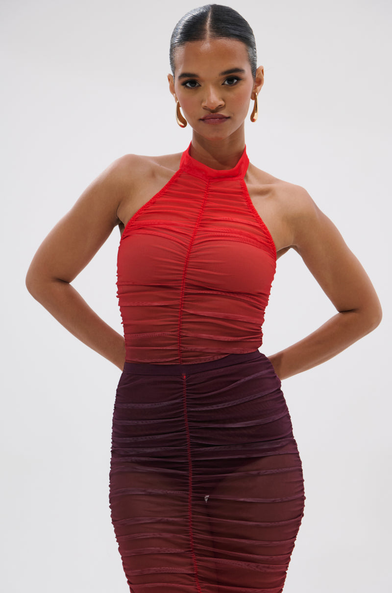 Wearing the OH FIRE OMBRE MESH BODYSUIT under a sleeveless red halter top and a ruched skirt, a woman with slicked-back hair stands confidently against a plain light background.