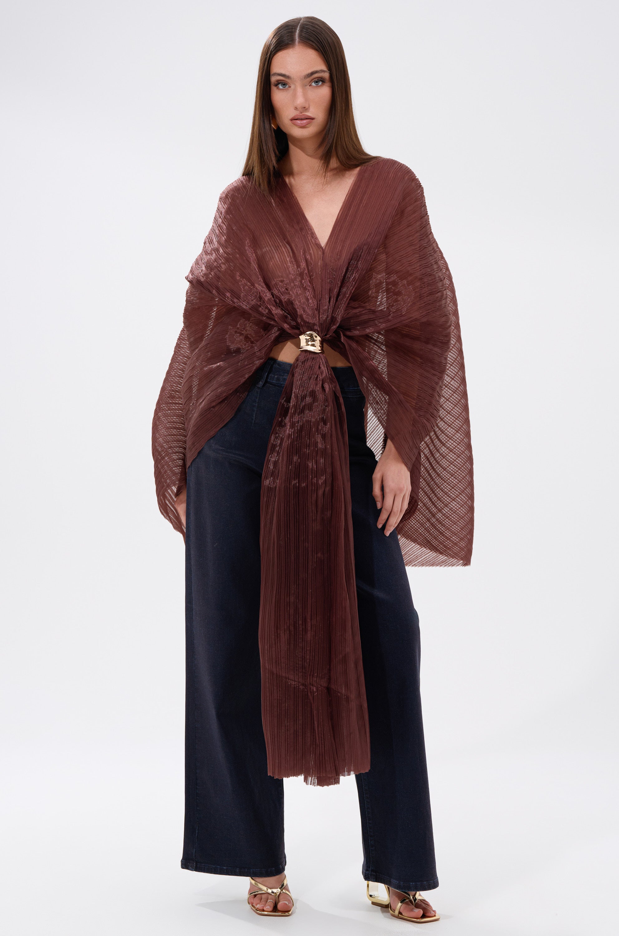 A woman wearing the FLY AWAY WITH ME BLOUSE IN BRONZE, a brown cape, and wide leg pants.