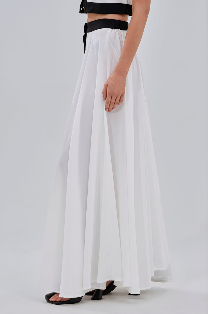 Wearing the VIVI MAXI SKIRT, paired with black open-toe heels and a black cropped top, someone stands against a plain light background, with only their lower half visible. 3