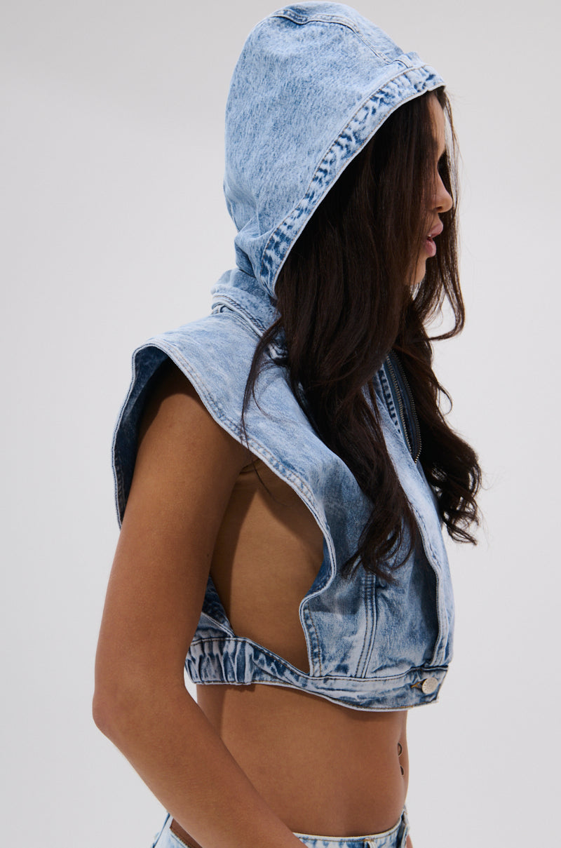 A woman with long dark hair models the TOO COOL FOR YOU DENIM ZIP-UP BLOUSE—a sleeveless, light blue cropped top with wide arm openings—showcasing a trendy streetwear style against a plain background. 4