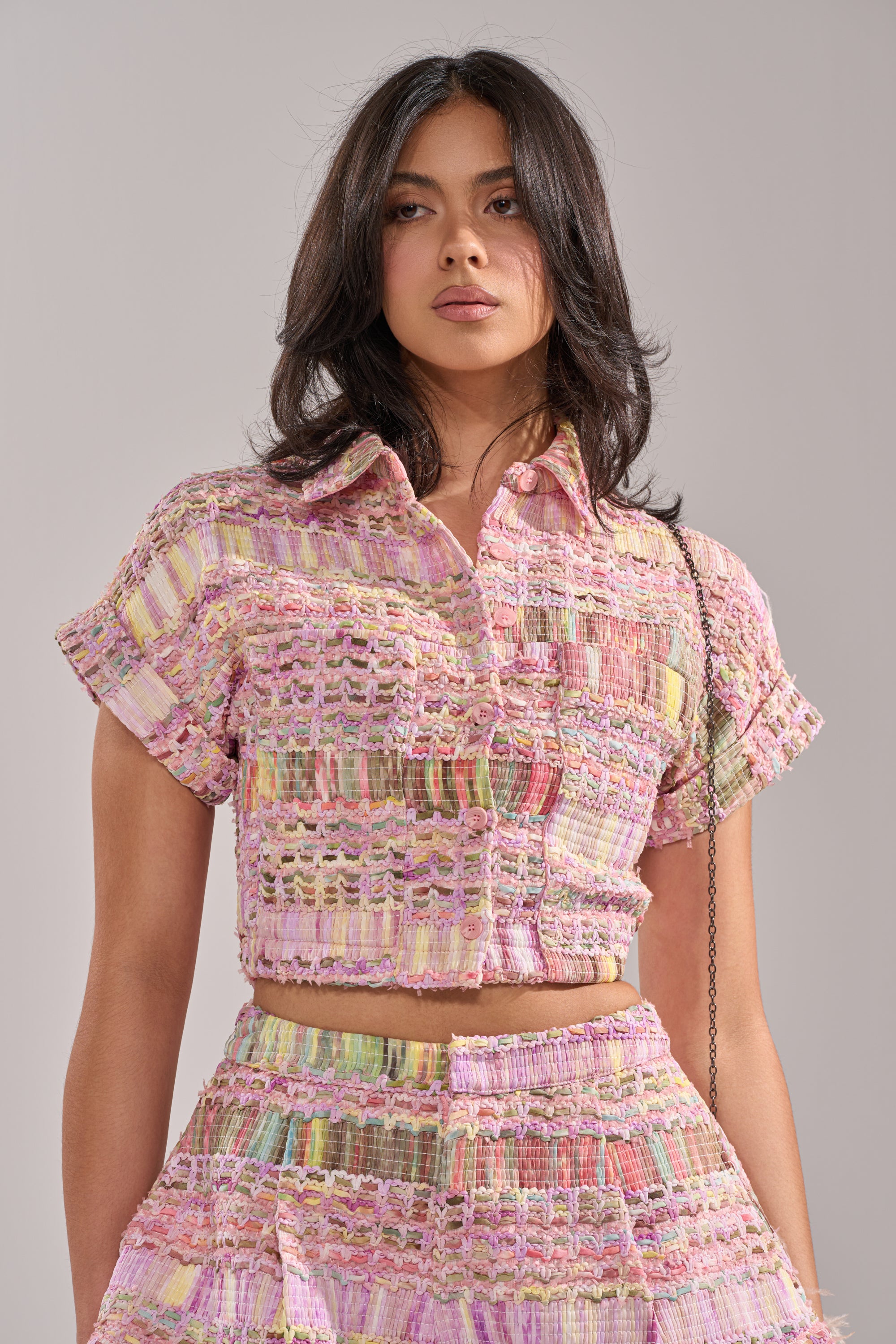 Wearing the VERONICA TWEED PLAID BLOUSE, a woman with long dark hair stands against a neutral background, confidently looking at the camera in her chic pastel ensemble. 0