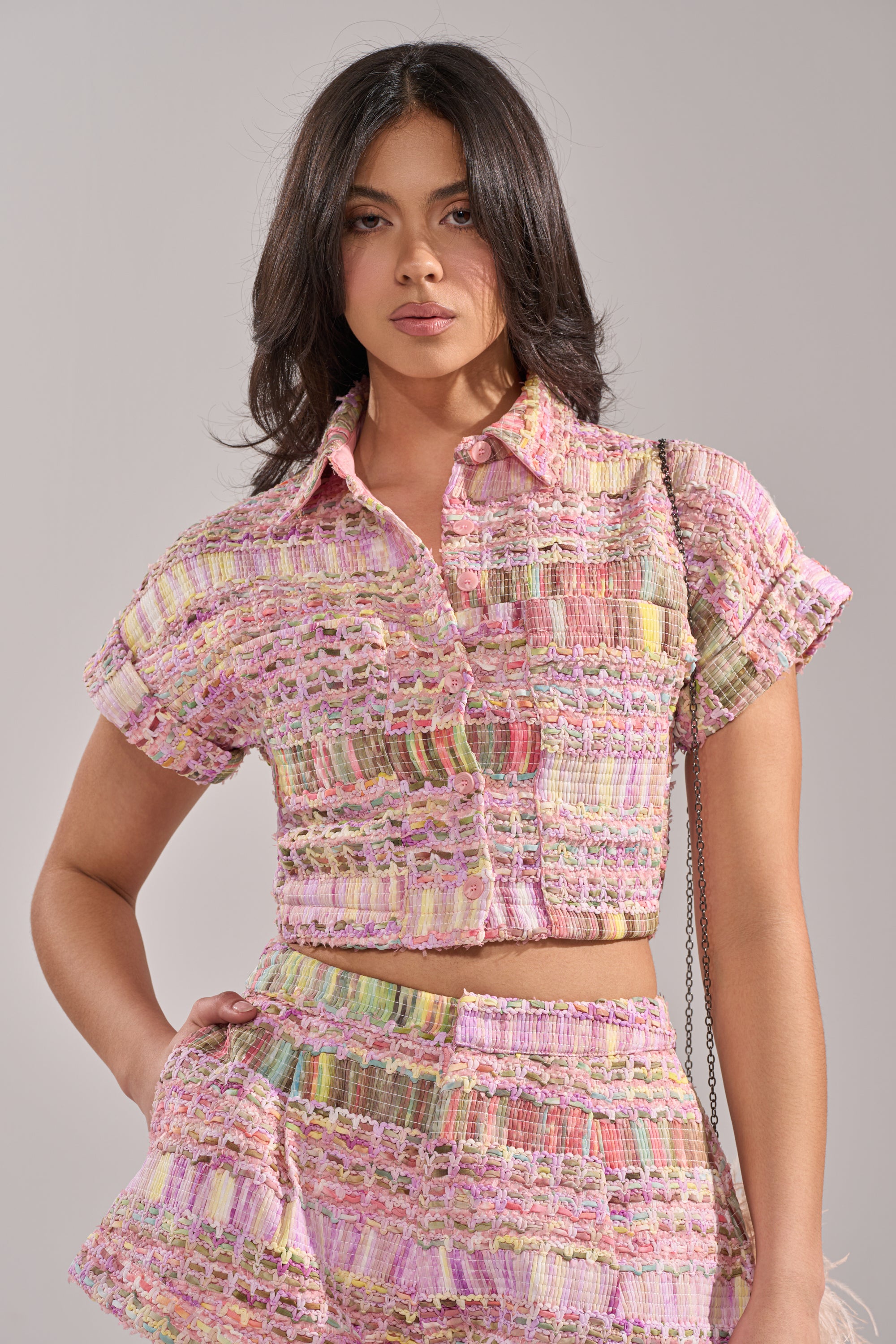 A woman with long dark hair models the chic VERONICA TWEED PLAID BLOUSE and matching high-waisted shorts, both featuring a pastel plaid woven pattern, standing confidently against a plain light background. 1