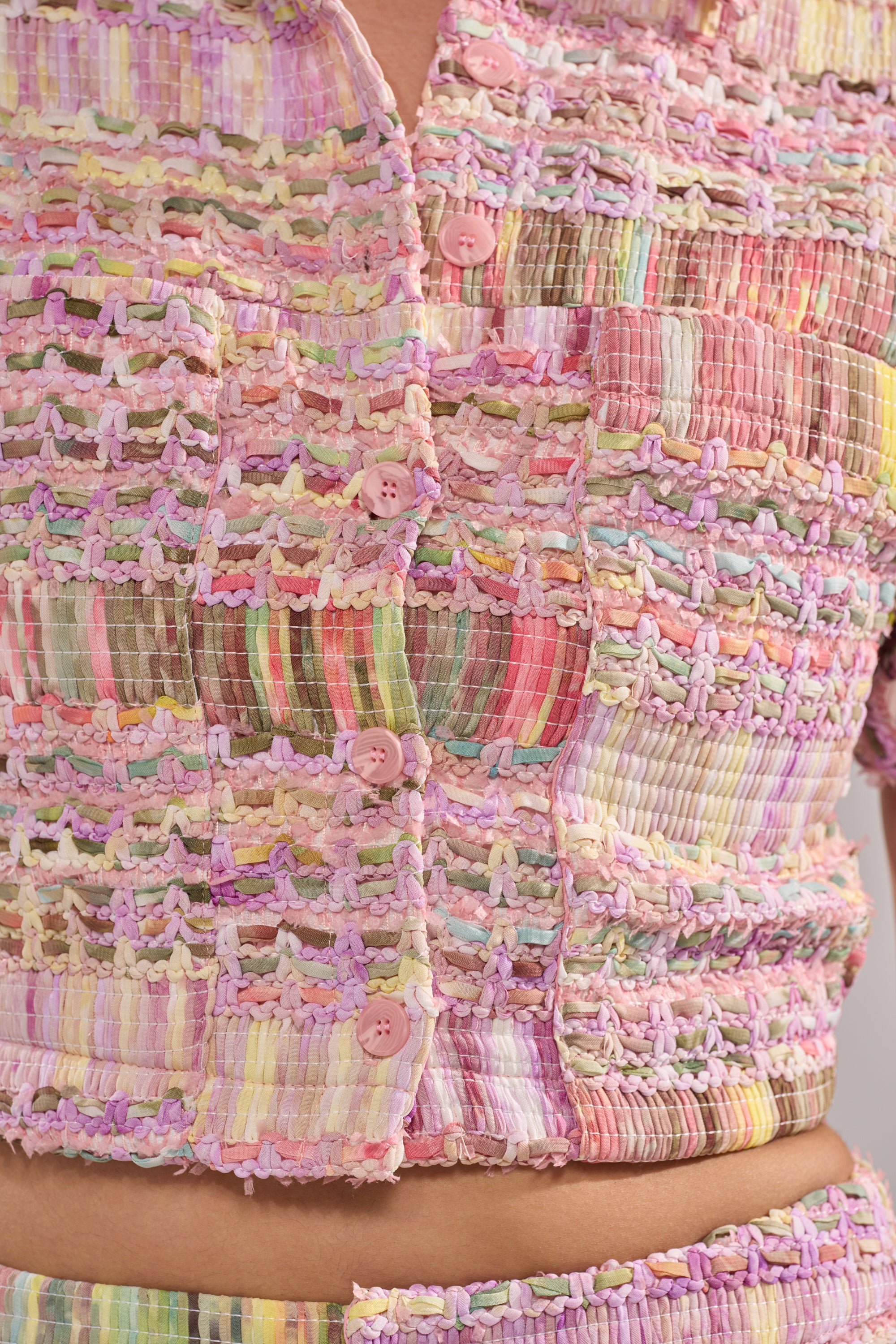 Close-up of the VERONICA TWEED PLAID BLOUSE, a textured multicolored tweed with pastel patchwork, pink buttons, and a cropped boxy fit that reveals the midriff for a playful look. 6