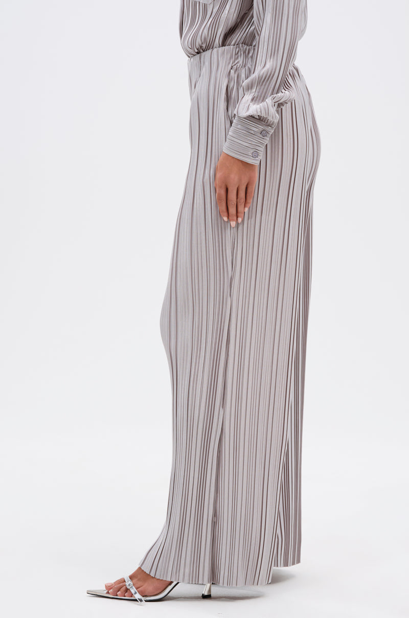 A person stands in profile against a white background, wearing the ALIA SLINKY PALAZZO PANT in light gray with vertical black stripes, paired with a matching satin-blend top and white heeled sandals. 3