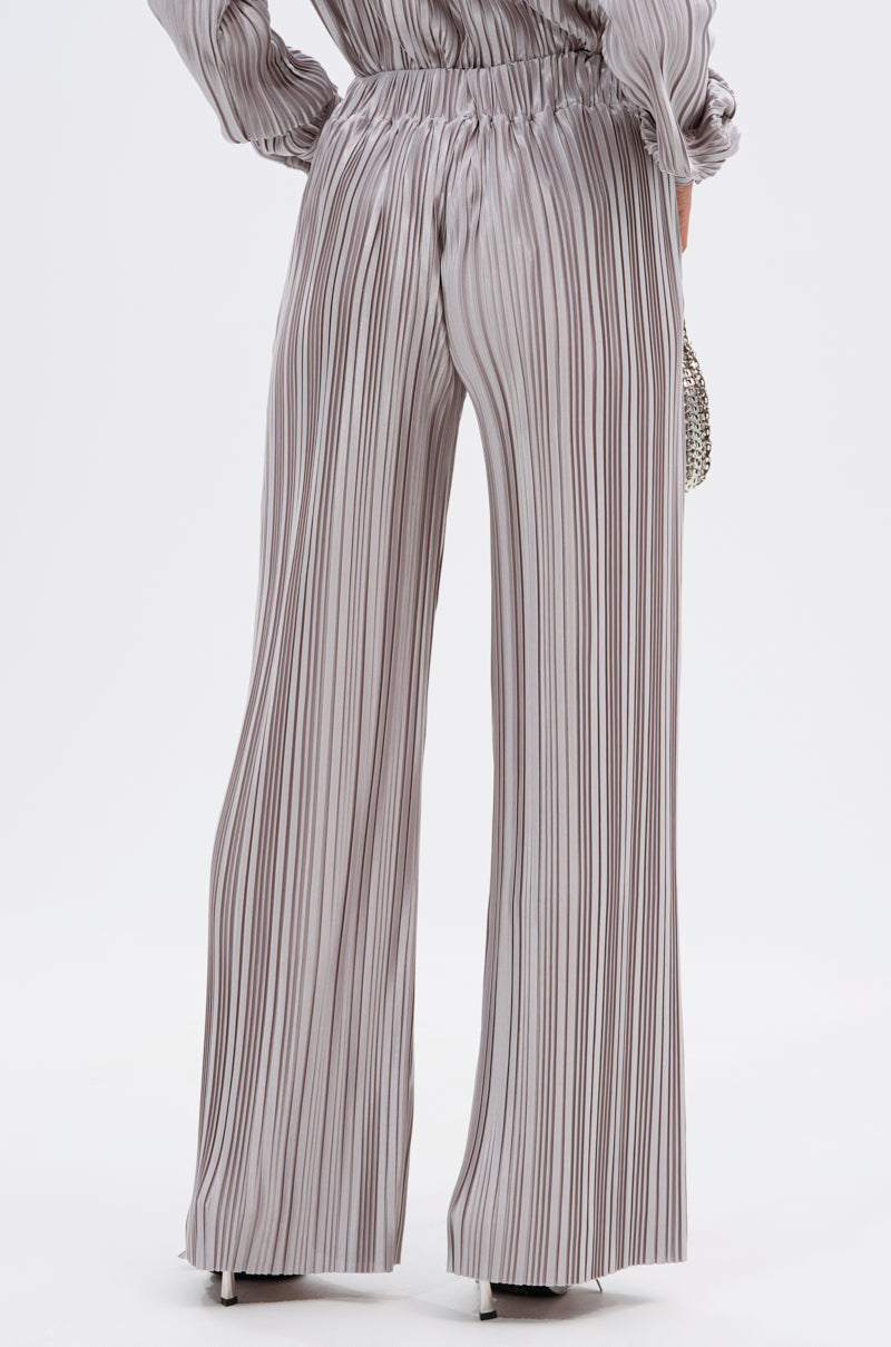 A person wears the ALIA SLINKY PALAZZO PANT, high-waisted with wide legs and vertical gray-and-white stripes, teamed with a matching pleated long-sleeve top and a small purse for a lightweight, stylish look. 4
