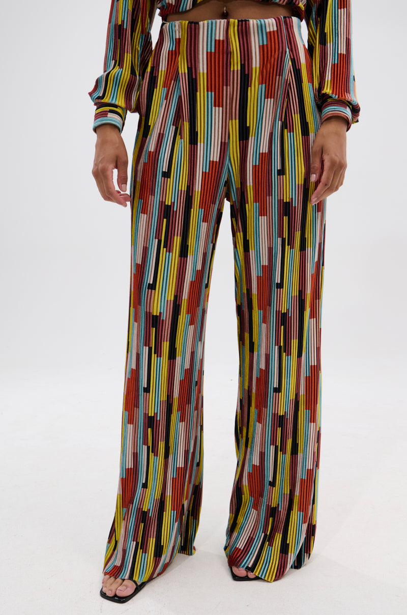 A person wears the VIBES FEEL GOOD VELVET PALAZZO PANT with a vibrant vertical stripe pattern and wide-leg silhouette, paired with a matching long-sleeve top. The photo shows the lower half of the outfit against a plain background. 1