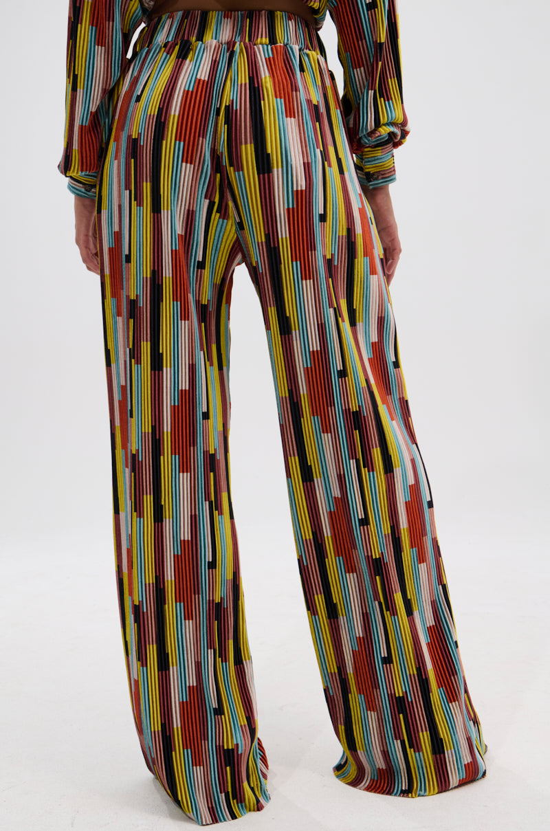 A person wears the VIBES FEEL GOOD VELVET PALAZZO PANT, featuring a high-waisted fit and vibrant multicolored stripes and block patterns. The back view highlights the wide-leg silhouette and lower half of the body. 4