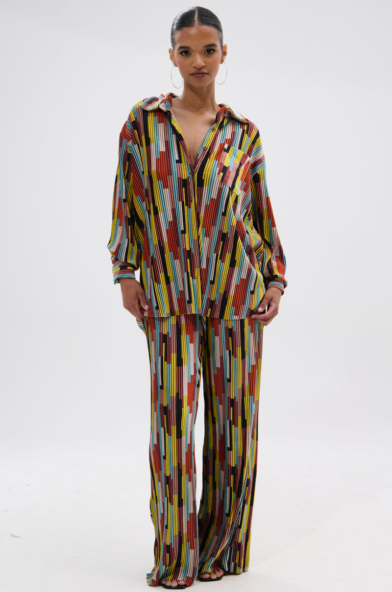 A person stands facing forward, wearing the VIBES FEEL GOOD VELVET PALAZZO PANT—a wide-leg, colorful two-piece set with vertical and rectangular geometric patterns in red, yellow, black, and white plus a matching button-up shirt. 5