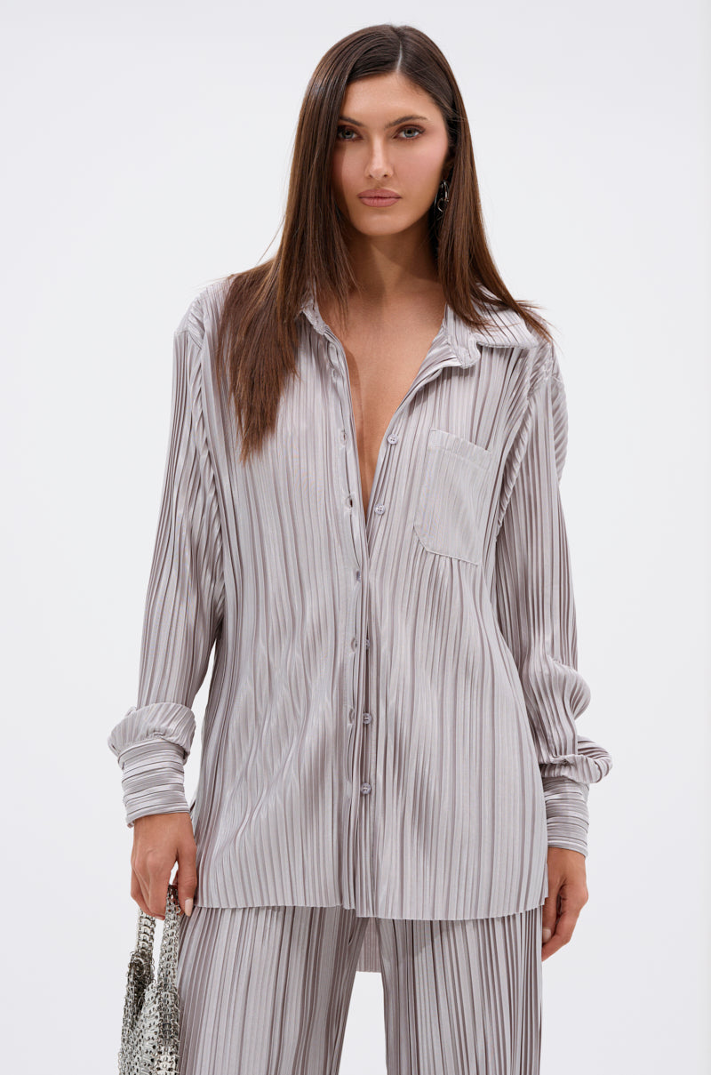 A woman stands against a plain background wearing the ALIA SLINKY BUTTON DOWN with vertical gray and white stripes, matching wide-leg pants, and holding a textured silver bag.