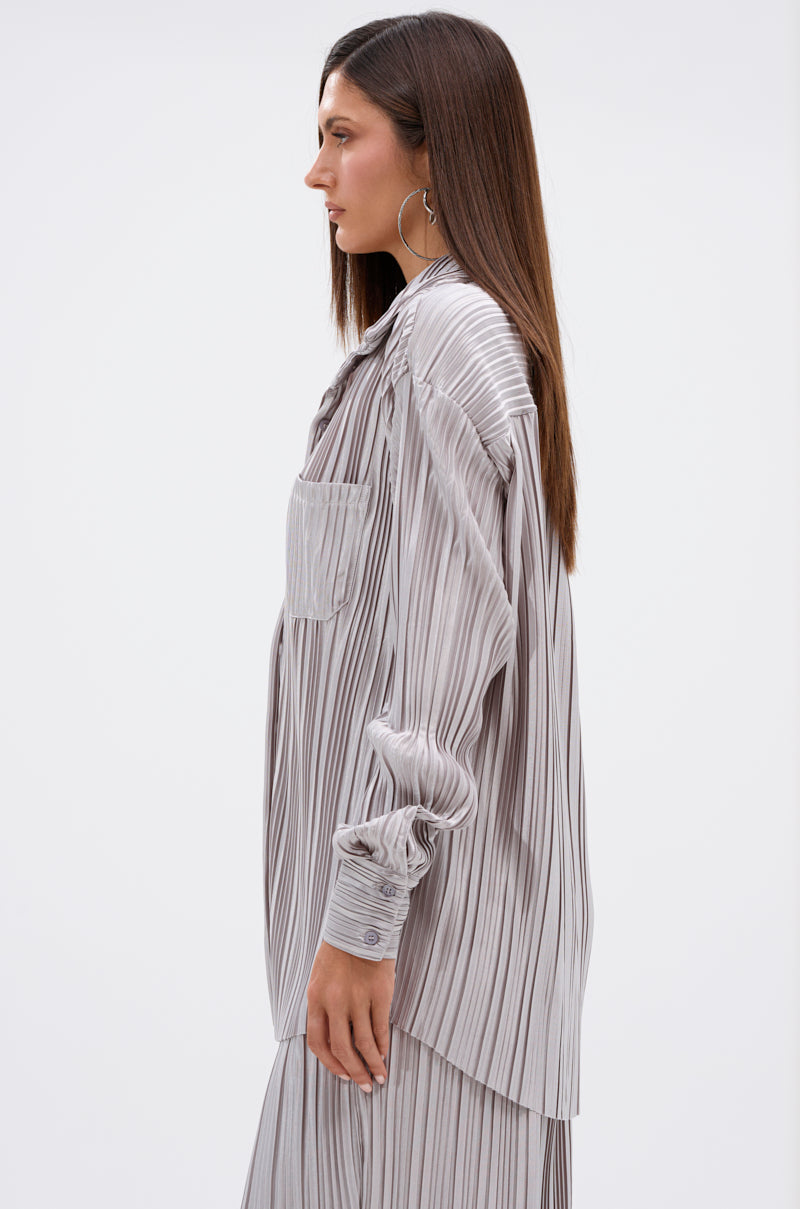 A woman with straight brown hair wears the ALIA SLINKY BUTTON DOWN in light gray with dark vertical stripes and a shimmering silver hue, shown in profile against a plain white background.