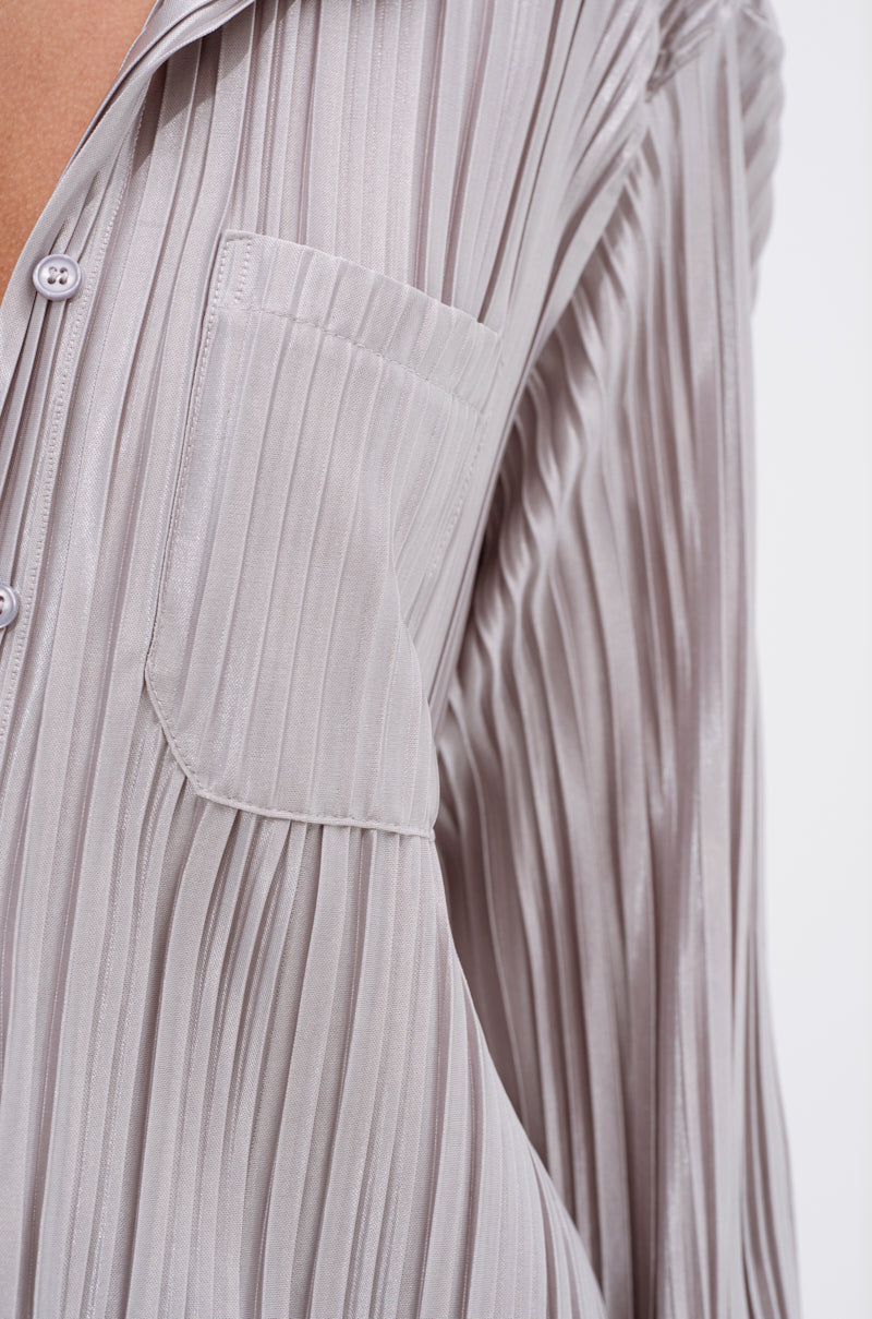 Close-up of the ALIA SLINKY BUTTON DOWN: a light gray, long-sleeve satin-blend shirt with pleats, chest pocket, button detail, and part of the collar shown against a plain white background.
