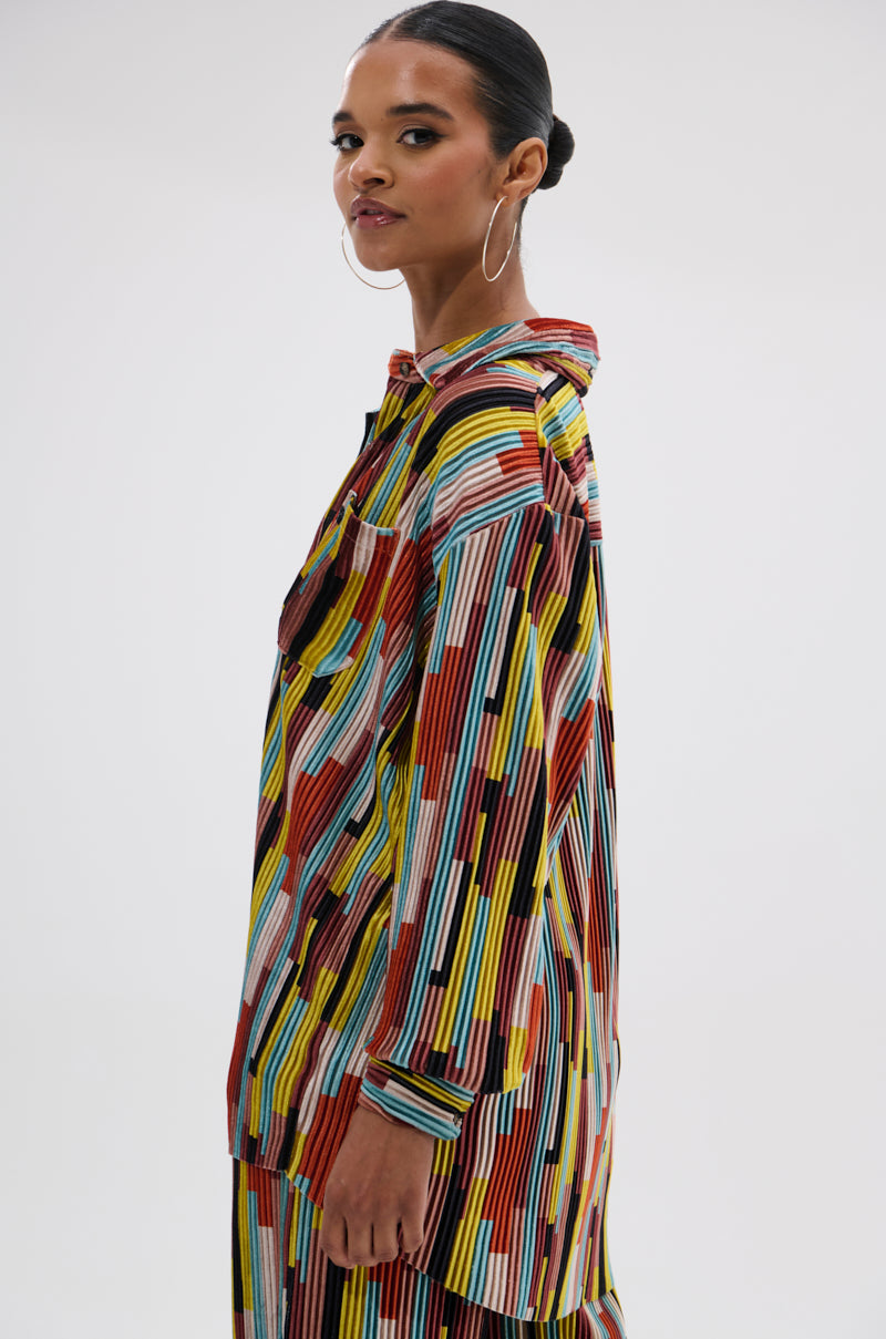 Wearing the VIBES FEEL GOOD VELVET COLOR BLOCKED BUTTON DOWN, a woman with hoop earrings and slicked-back hair stands sideways, confidently facing the camera against a plain background. 1