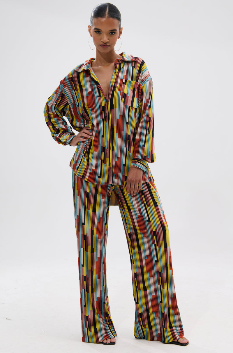 A woman models the VIBES FEEL GOOD VELVET COLOR BLOCKED BUTTON DOWN—a retro set with a loose, long-sleeve shirt and wide-leg pants featuring bold red, yellow, white, blue, and black geometric stripes. 4