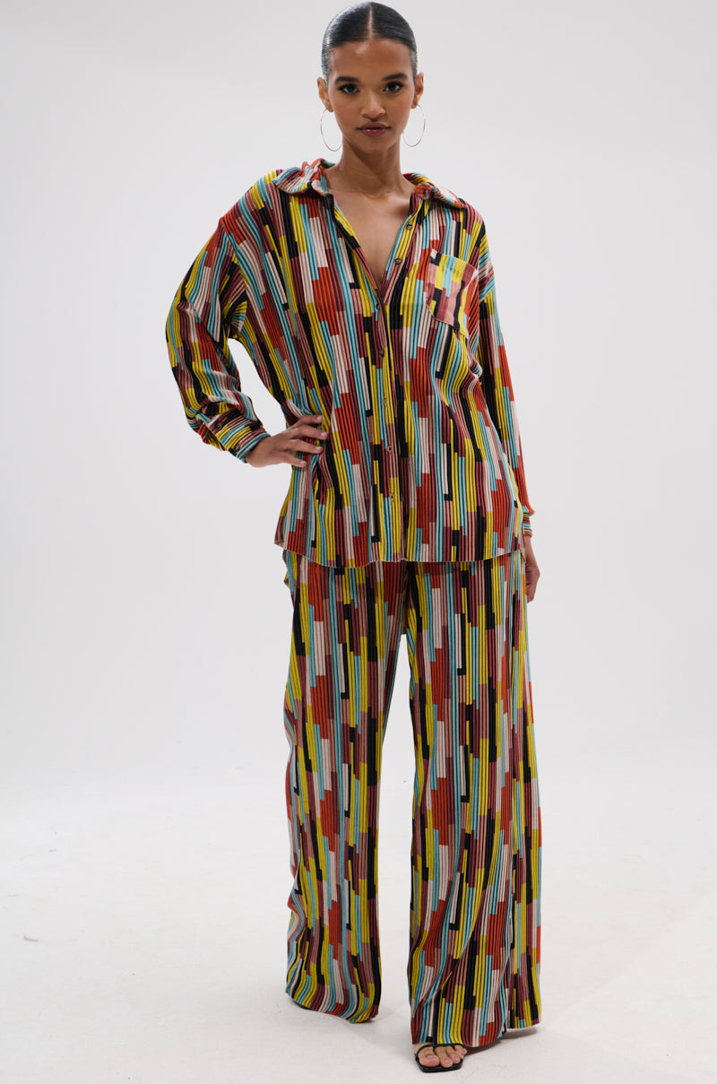 A woman stands confidently in the VIBES FEEL GOOD VELVET COLOR BLOCKED BUTTON DOWN with vertical stripes. She pairs it with hoop earrings, slicked-back hair, and black open-toe heels against a white background. 5