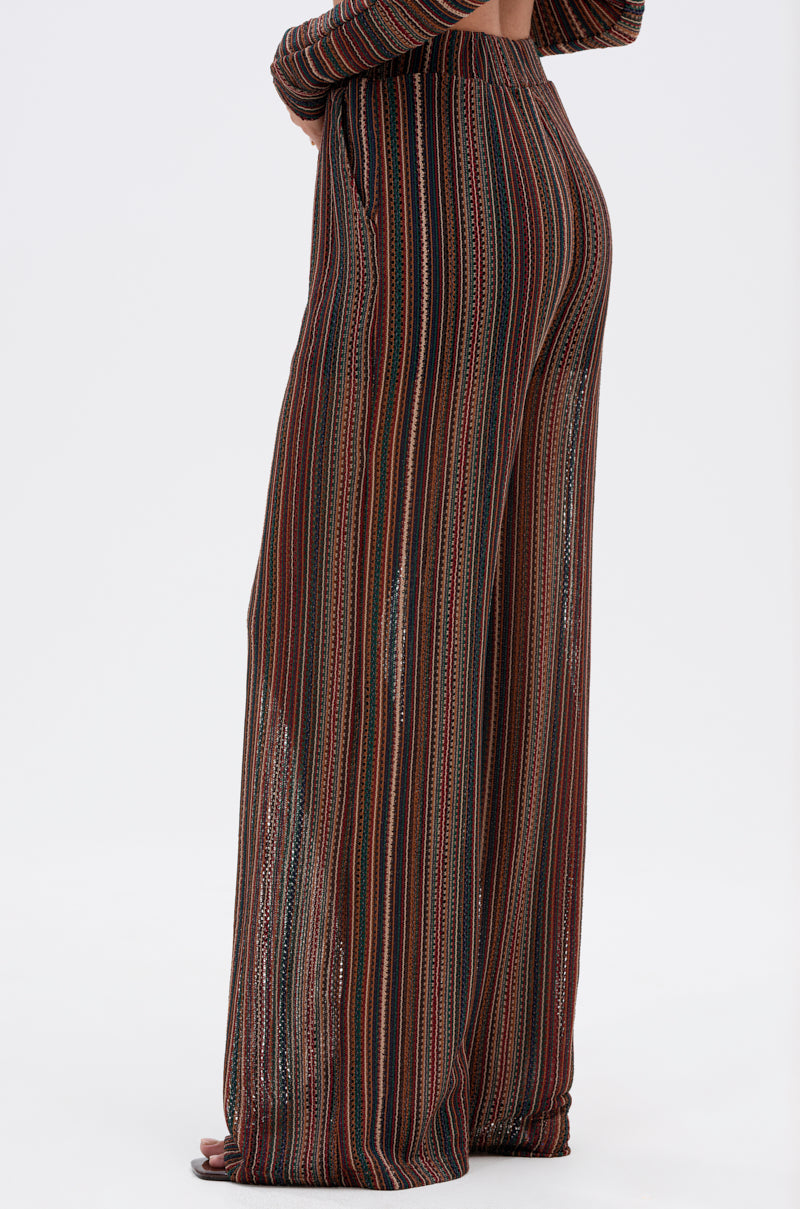 A person models the CANDICE STRIPE WIDE LEG PANT, showcasing its boho-chic, relaxed fit and multicolored vertical stripes against a plain white background, with partially visible feet. 2
