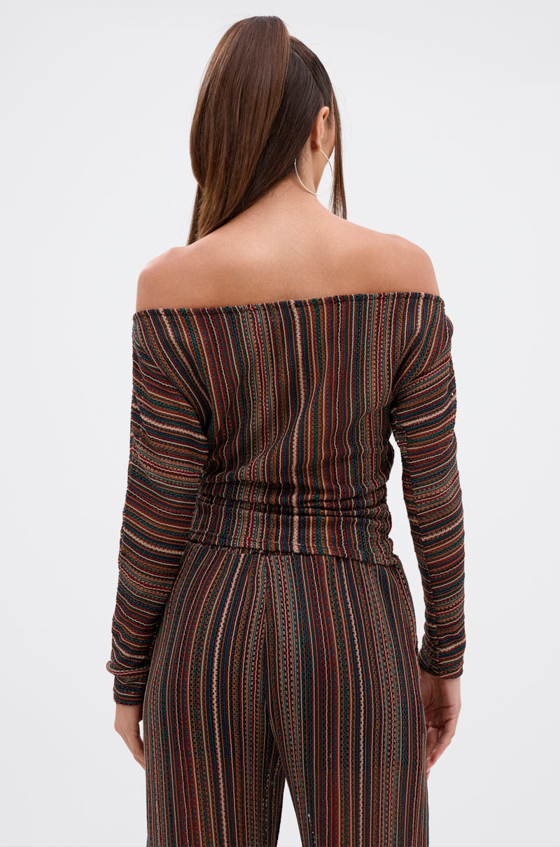 A woman with a high ponytail, facing away, wears the CANDICE STRIPE OFF THE SHOULDER BLOUSE and matching multicolored striped pants against a plain white background. 3