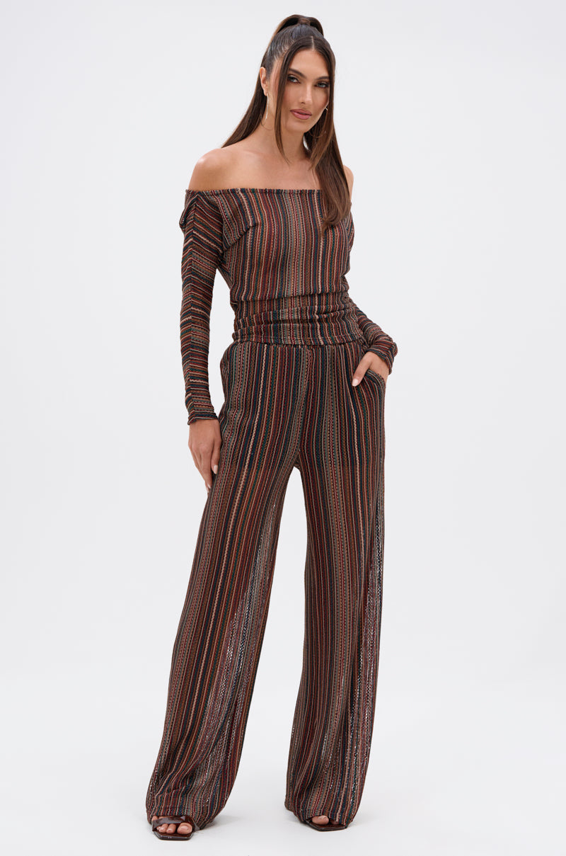 A woman stands confidently against a white background wearing the CANDICE STRIPE OFF THE SHOULDER BLOUSE, featuring vertical multicolored stripes, long sleeves, wide-leg pants style, and convenient side pockets. 5