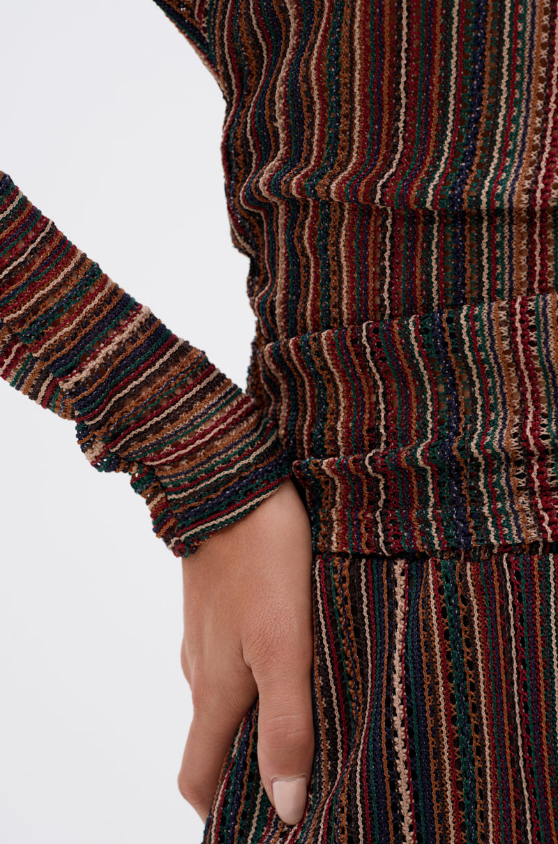 A close-up of a hand on a hip, wearing the CANDICE STRIPE OFF THE SHOULDER BLOUSE featuring textured, ribbed fabric with multicolored vertical stripes in earthy tones. 6