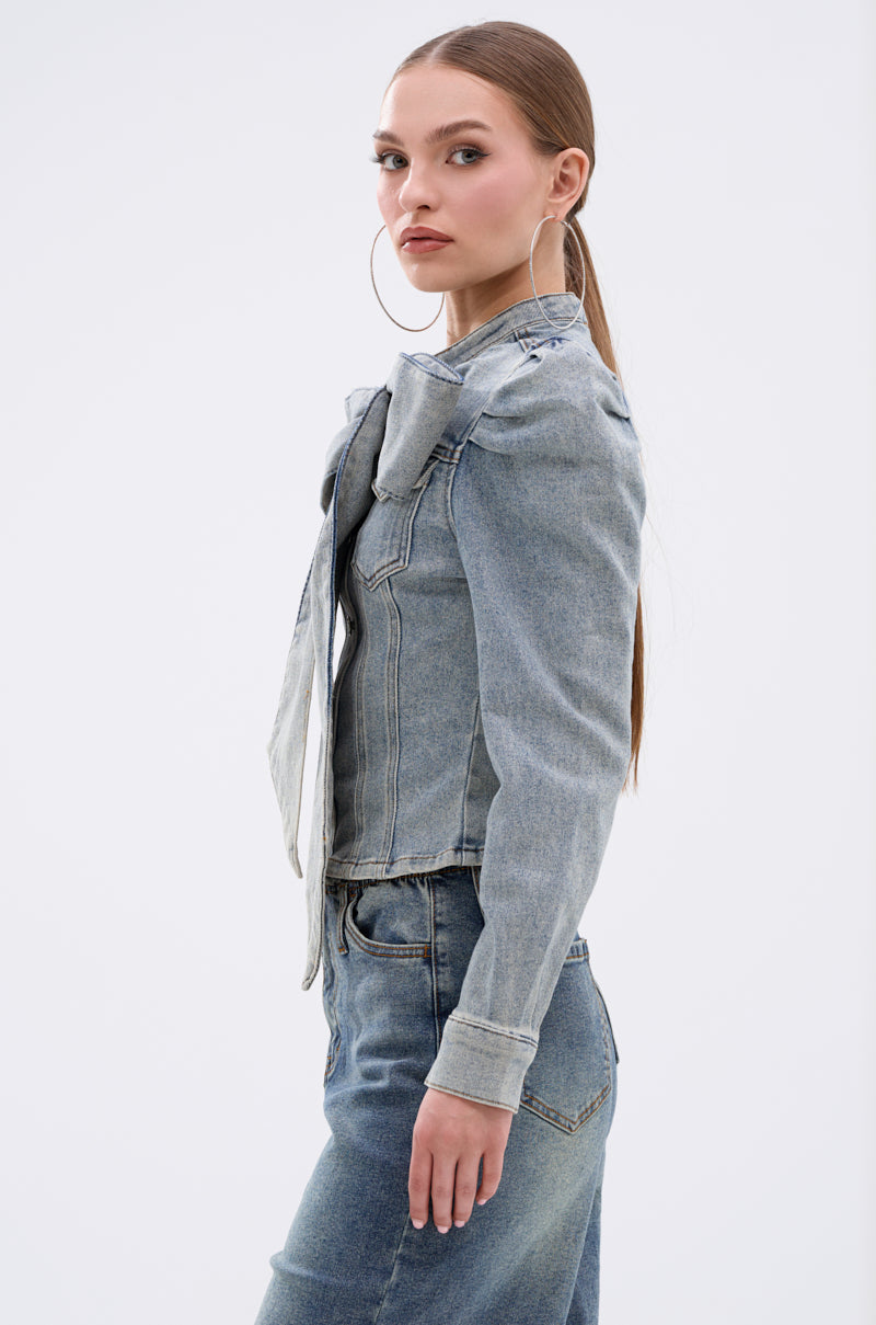 A woman with long brown hair in a low ponytail, large hoop earrings, and the WAIT FOR U DENIM BOW BLOUSE TOP stands in profile against a plain white background.
