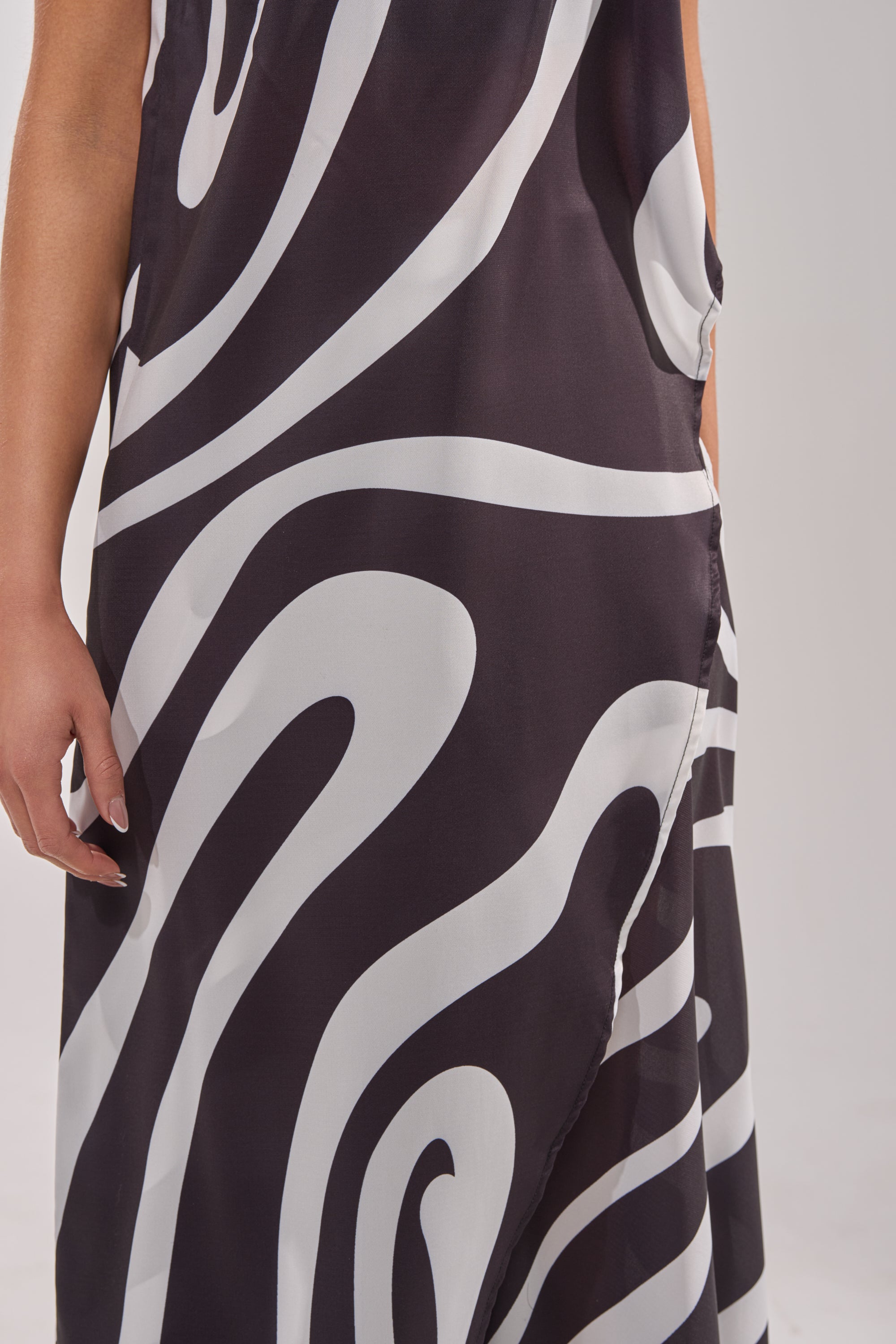 A close-up of a person wearing the TRINA ELONGATED SINGLE SHOULDER TOP in black with bold black and white swirl print; their left arm is visible. The top features a pocket, making it a true statement piece. 6