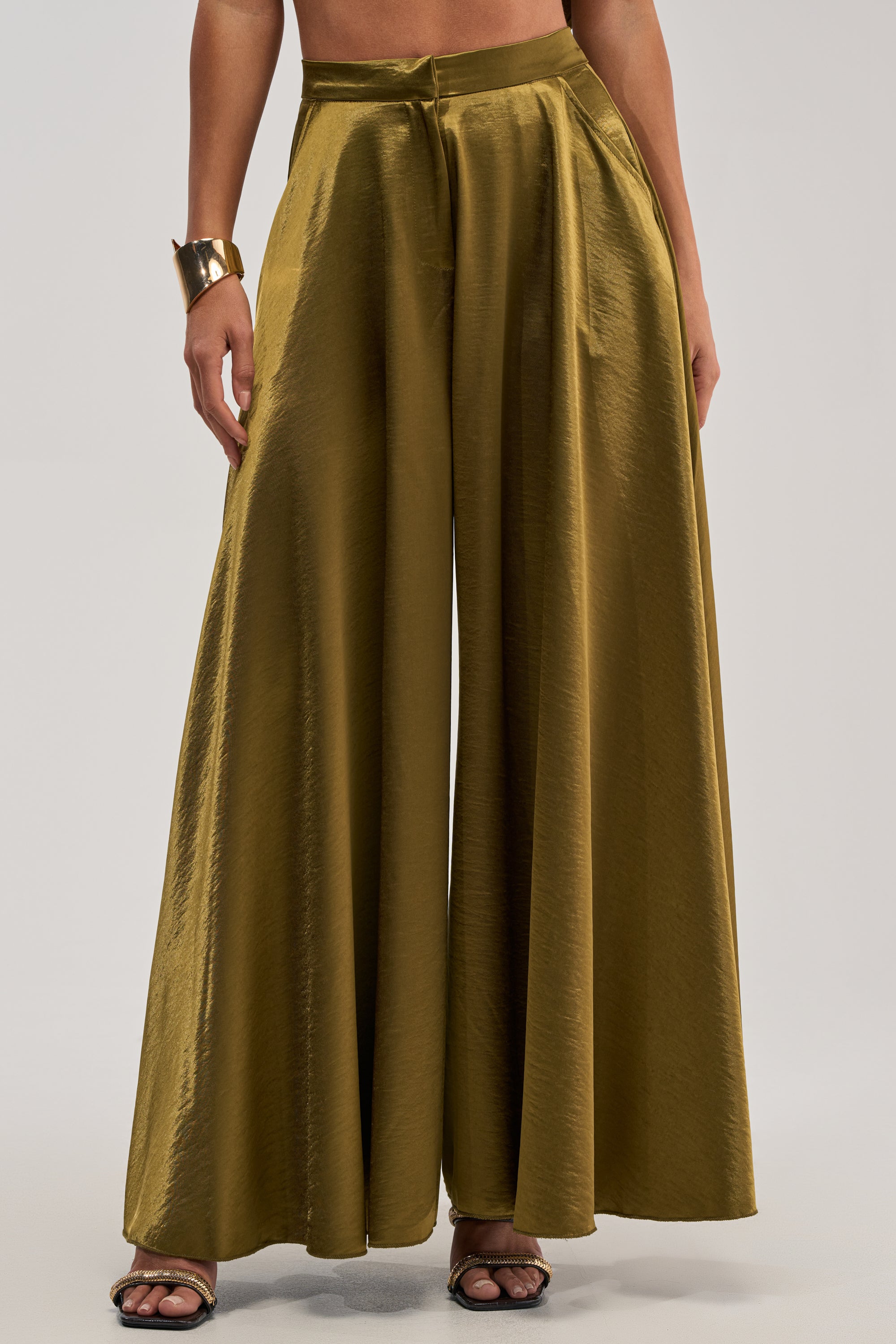 A person in TRUE GODDESS GREEN PALAZZO PANT with a wide-leg silhouette, black open-toe heels, and a chunky metallic bracelet stands against a plain background—a chic choice for elegant event dressing.