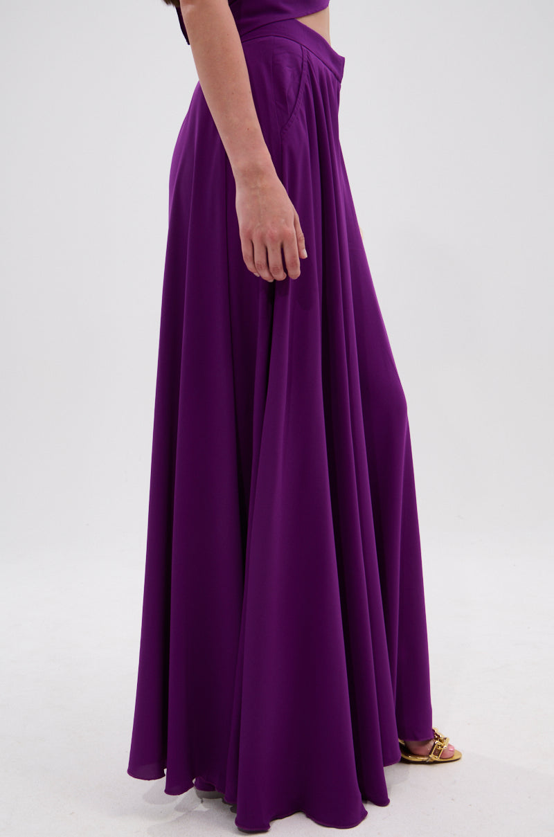 A person models the TRINA PLEATED PALAZZO PANT in a high-rise, violet shade with gold sandals, standing against a plain white background. Only their lower body is visible. 3