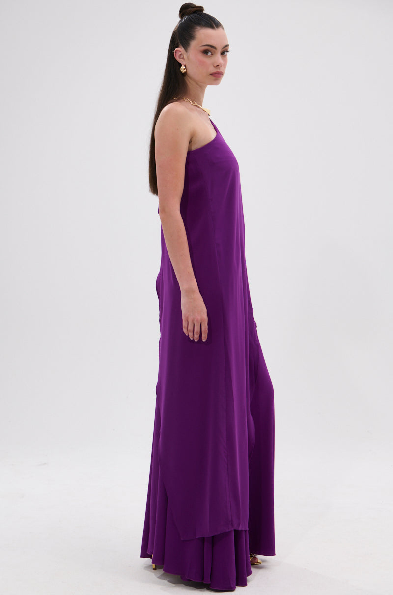 A woman with long dark hair in a high ponytail models the TRINA ELONGATED SINGLE SHOULDER TOP, standing sideways against a plain white background and looking toward the camera. 5