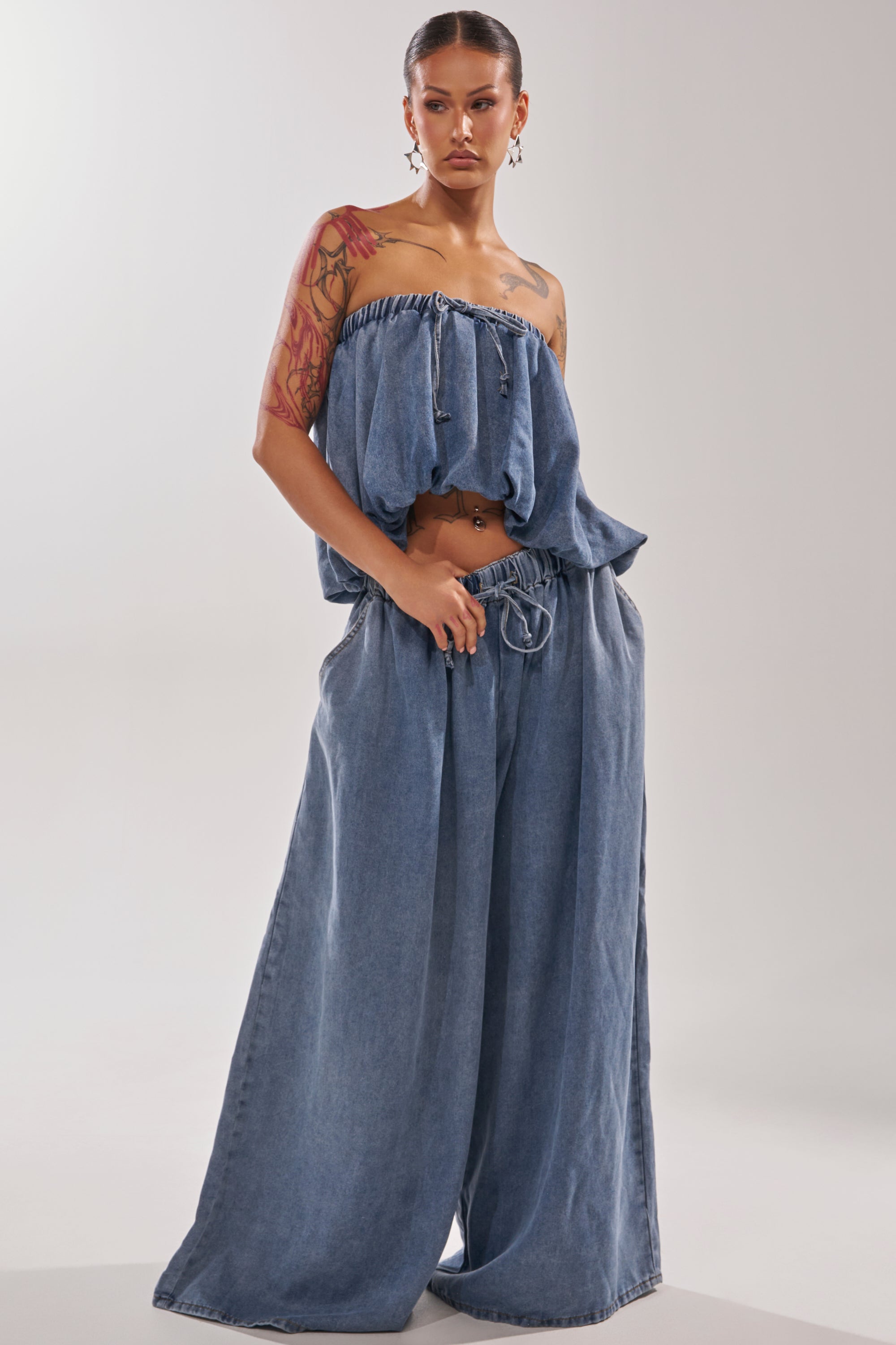 A woman with tattoos poses confidently in the DENIM FOR DAYS JOGGER, featuring a strapless, loose-fitting denim top and high-rise wide-leg denim pants, against a plain background. 6