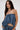 A woman with long brown hair wears the DENIM FOR DAYS TUBE TOP by AKIRA Label, featuring gathered, ruched denim fabric and matching pants. She stands against a white background, looking confidently at the camera.