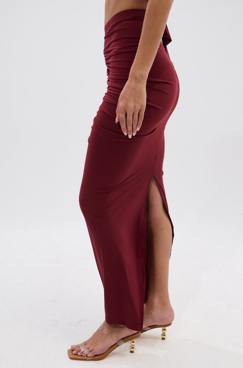A person wearing the SEXY RUCHED BACK SLIT MAXI SKIRT in high-rise burgundy, styled with open-toe sandals featuring gold ball heels, stands against a plain light background. 4