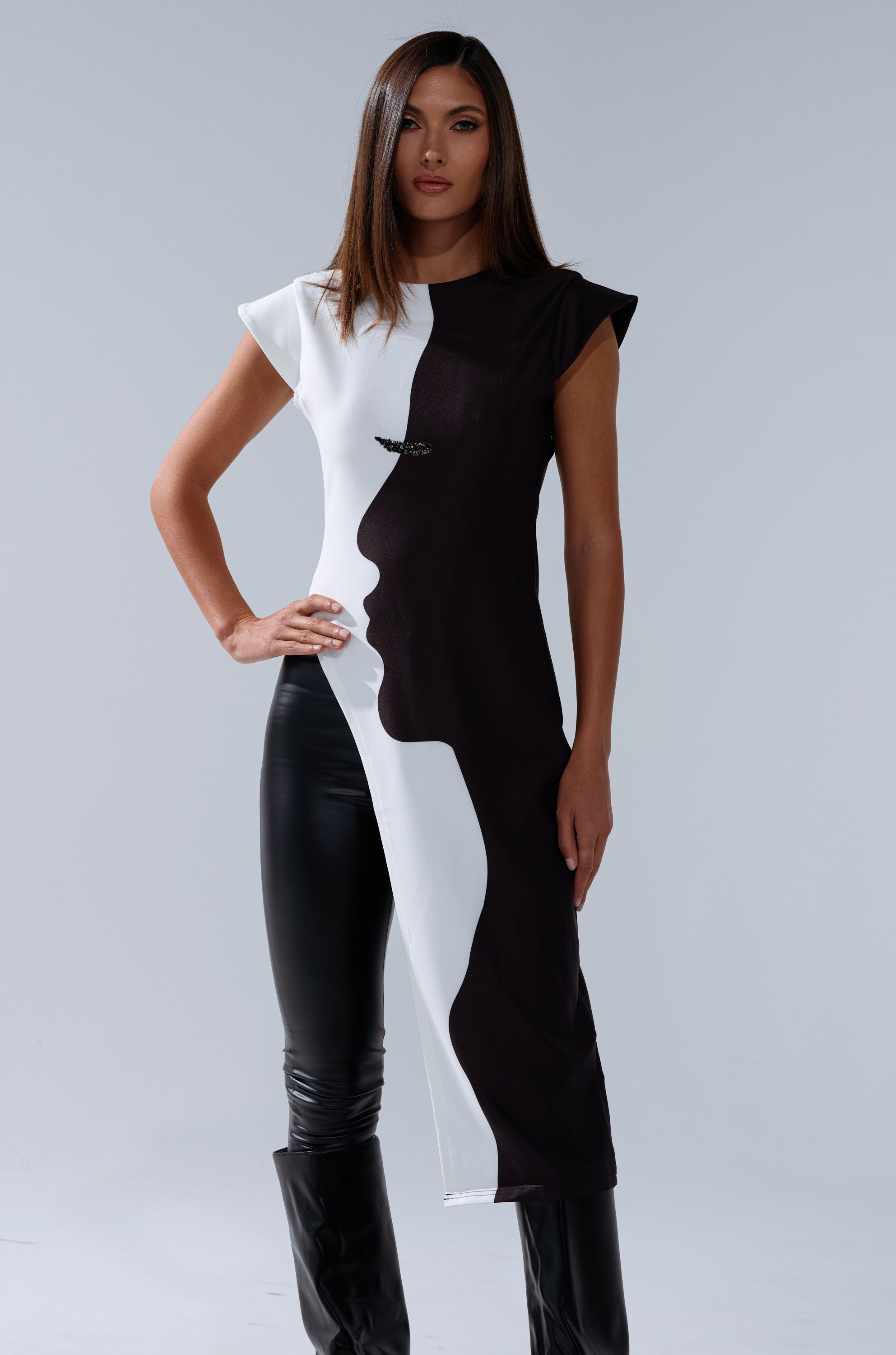 A woman exudes confidence in the SILHOUETTE LONGLINE TEE, featuring bold two-tone colors that create abstract face profiles. She styles this unique tee with black pants and boots for a striking look.