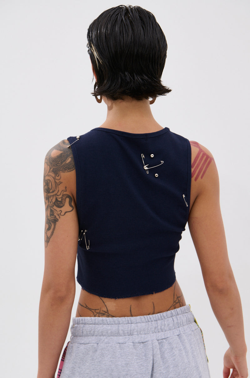 A person with short, dark, wet-look hair is seen from behind wearing a BOYS LIE DISTRESSED CROPPED TANK TOP and gray sweatpants. Tattoos cover their left arm and shoulder. The plain light background gives a punk-inspired vibe. 2