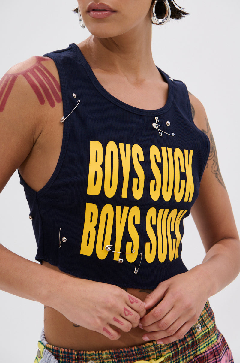 A person with short hair, hoop earrings, tattoos, and colorful plaid pants wears the BOYS LIE DISTRESSED CROPPED TANK TOP—a ribbed cotton-blend with yellow "BOYS SUCK" text, safety pins, and a punk-inspired look. 5