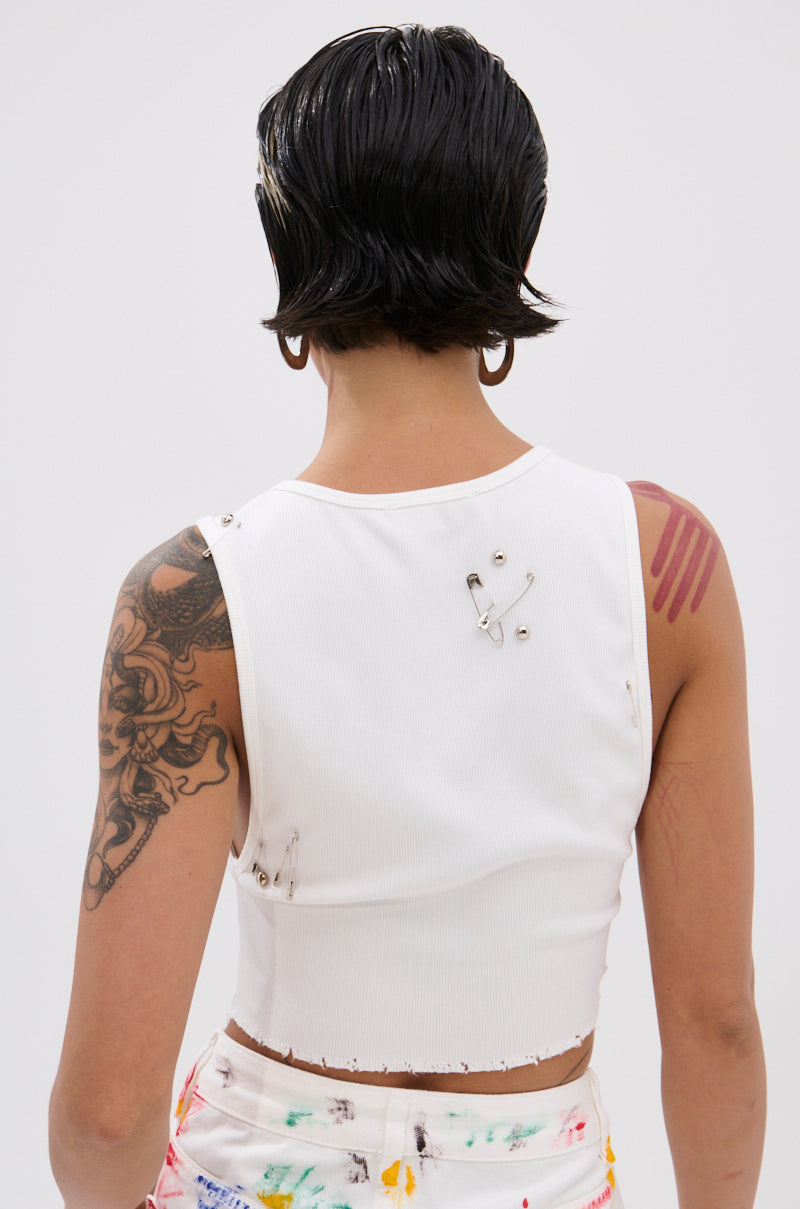 A person with short dark hair, seen from behind, is wearing the NEVER CARED DISTRESSED CROPPED TANK TOP and colorful pants, showing a large tattoo on their left arm and a pink mark on their right shoulder. 2