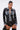 A woman with slicked-back hair wears the MIXED VIBES FAUX LEATHER BUTTON DOWN with denim trim, black high-waisted lace bottoms, hoop earrings, and a studded black handbag. She poses against a plain white background.