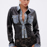 A woman with slicked-back hair wears the MIXED VIBES FAUX LEATHER BUTTON DOWN with denim trim, black high-waisted lace bottoms, hoop earrings, and a studded black handbag. She poses against a plain white background.