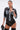 A woman stands confidently against a plain background, wearing the MIXED VIBES FAUX LEATHER BUTTON DOWN with denim trim, black lace underwear, large hoop earrings, a silver cuff bracelet, and holding a black studded accessory.