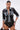 Wearing the MIXED VIBES FAUX LEATHER BUTTON DOWN and lace black shorts, a woman poses confidently with hoop earrings and chunky bracelets against a plain white background.
